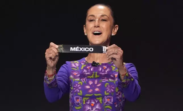 Mexican President Claudia Sheinbaum holds up the team name of Mexico during the draw for the 2026 soccer World Cup at the Kennedy Center in Washington, Friday, Dec. 5, 2025.(AP Photo/Evan Vucci)