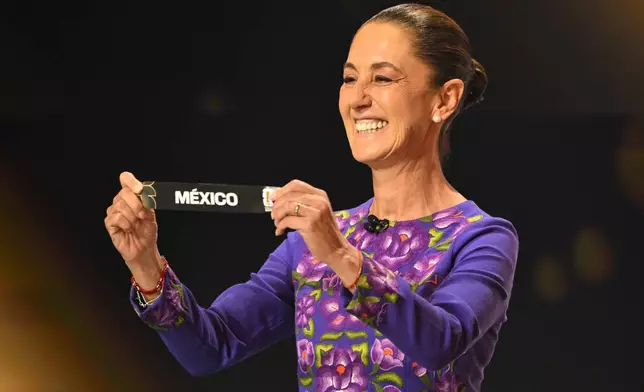 Mexican President Claudia Sheinbaum holds up Mexico after drawing from a pot during the draw for the 2026 soccer World Cup at the Kennedy Center in Washington, Friday, Dec. 5, 2025. (Mandel Ngan/Pool Photo via AP)