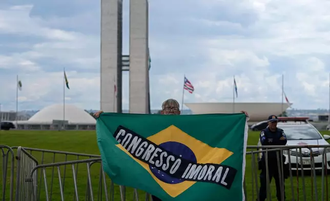 A demonstrator carries a Brazilian flag with the phrase, "Immoral Congress" in Portuguese in front of Congress during a protest against a bill that looks to reduce former President Jair Bolsonaro's prison time, in Brasilia, Brazil, Sunday, Dec. 14, 2025. (AP Photo/Eraldo Peres)