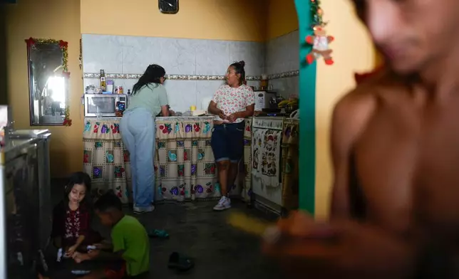 Mariela Gómez, a Venezuelan migrant who abandoned her journey with her children to the United States following President Donald Trump's immigration crackdown, chats with a relative while cooking Christmas dinner in Maracay, Venezuela, Friday, Dec. 24, 2025. (AP Photo/Matias Delacroix)