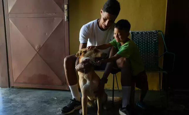 Abraham Castro and his partner's son Mathias pet the family dog ahead of Christmas Eve celebrations in Maracay, Venezuela, Thursday, Dec. 24, 2025. The Venezuelan migrant family adopted the dog as a puppy in Mexico before abandoning their journey to the United States and returning home following President Donald Trump's immigration crackdown. (AP Photo/Matias Delacroix)