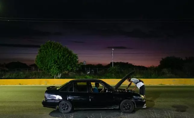 Abraham Castro helps fix the taxi taking him and his partner, Mariela Gómez, to his parents' home for Christmas dinner in Maracay, Venezuela, Wednesday, Dec. 24, 2025. The Venezuelan migrant couple abandoned their journey to the United States and returned home from Mexico by land and sea following the immigration crackdown under President Donald Trump. (AP Photo/Matias Delacroix)