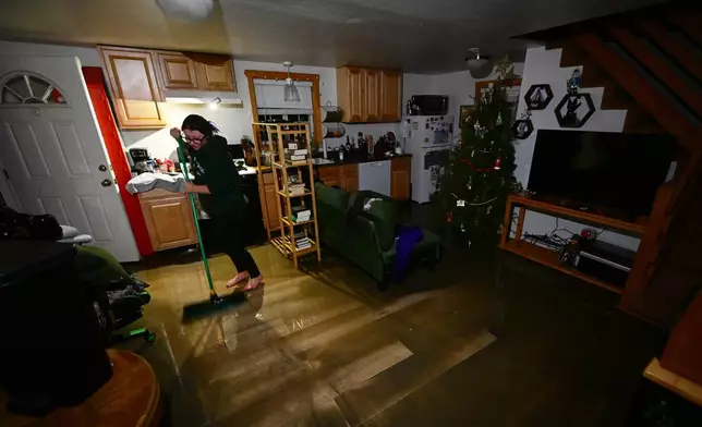 A resident sweeps water and mud in her house after flooding Wednesday, Dec. 24, 2025, in Wrightwood, Calif. (AP Photo/Wally Skalij)