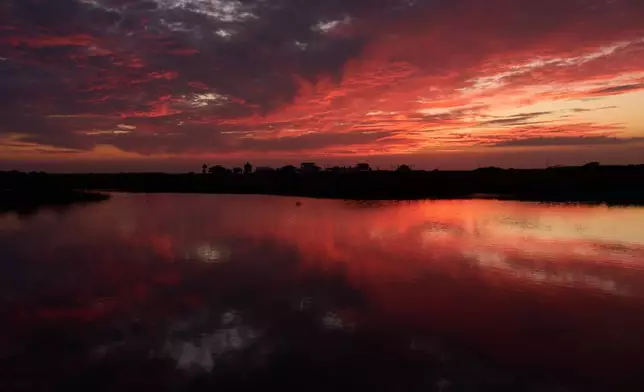 Clouds illuminated by the setting sun are reflected in water at the Wolfberry Whooping Crane Sanctuary, Friday, Dec. 12, 2025, near Seadrift, Texas. (AP Photo/John Locher)