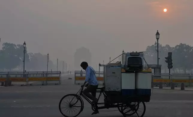 FILE - A cyclist pedals through morning smog near the India Gate monument as he transports used home appliances in New Delhi, India, Oct. 21, 2025. (AP Photo/Manish Swarup, File)