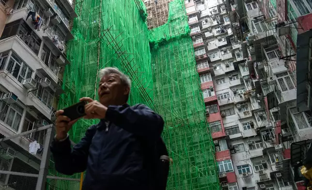 People walk past the building under renovation in Quarry Bay district after the deadly fire at Wang Fuk Court, in the Tai Po district of Hong Kong's New Territories, Thursday, Dec 4, 2025. (AP Photo/Chan Long Hei)