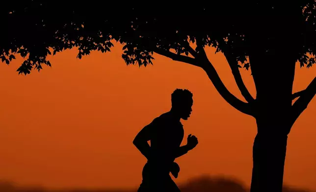 FILE - A man is silhouetted against the sky at sunset as he jogs in a park at the close of a hot summer day, Aug. 1, 2022, in Kansas City, Mo. (AP Photo/Charlie Riedel, File)