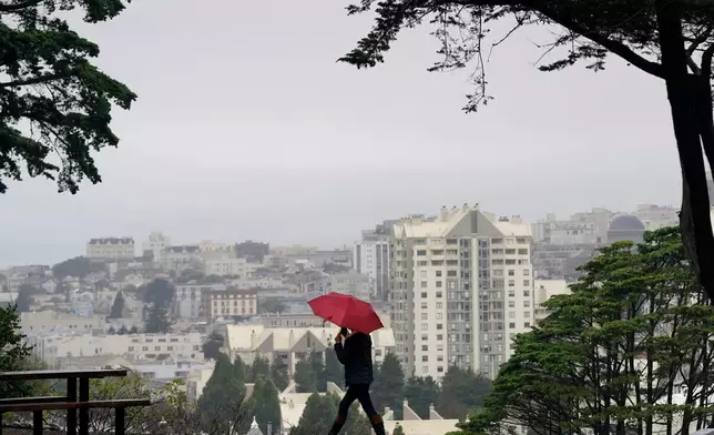 FILE - A woman carries an umbrella while walking at Alamo Square Park in San Francisco, Nov. 9, 2021. (AP Photo/Jeff Chiu, File)