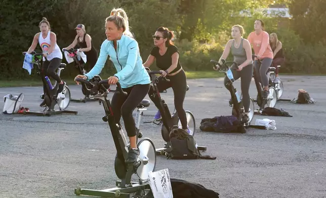 FILE - Jackie Brennan, of Merrimac, Mass., front, pedals on a stationary exercise bike with others during a spinning class in a parking lot outside Fuel Training Studio,Sept. 21, 2020, in Newburyport. (AP Photo/Steven Senne, File)