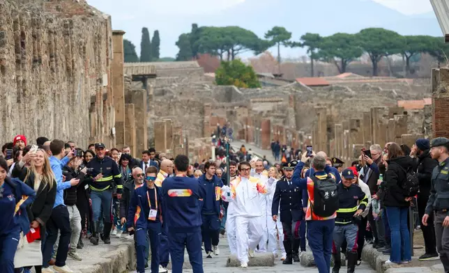 Actor Jackie Chan holds the olympic torch passing through the Archaeological Park in Pompeii, Italy, Monday, Dec. 22, 2025. (Alessandro Garofalo/LaPresse via AP)