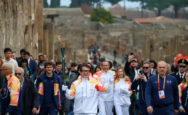 Actor Jackie Chan holds the olympic torch passing through the Archaeological Park in Pompeii, Italy, Monday, Dec. 22, 2025. (Alessandro Garofalo/LaPresse via AP)