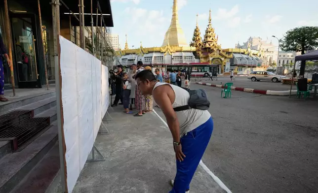 A man looks for his name on voter lists displayed outside a polling station, with Sule Pagoda in background, Sunday, Dec. 28, 2025, in Yangon, Myanmar. (AP Photo/Thein Zaw)