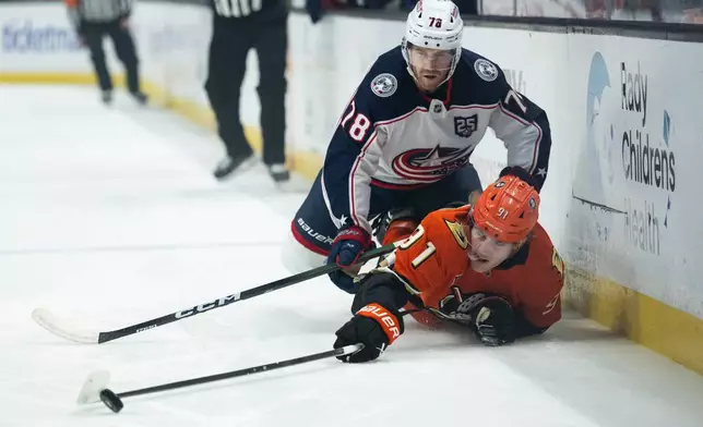 Anaheim Ducks center Leo Carlsson (91) reaches for the puck as Columbus Blue Jackets defenseman Damon Severson (78) checks him during the first period of an NHL hockey game, Saturday, Dec. 20, 2025, in Anaheim, Calif. (AP Photo/Kyusung Gong)