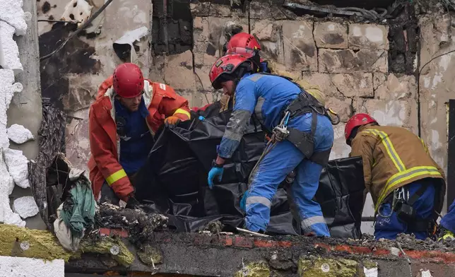 Rescuers put remains of a body of a victim into a plastic bag after Russian drone hit a multi-storey apartment building during massive missile and drone attack in Kyiv, Ukraine, Saturday, Dec. 27, 2025. (AP Photo/Efrem Lukatsky)