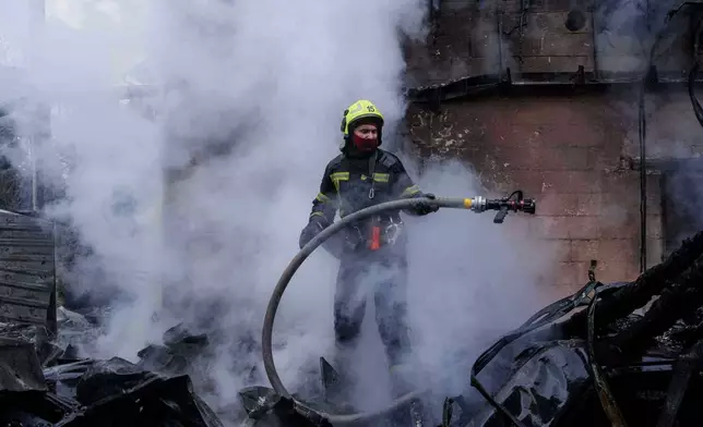 A rescue worker puts out a fire of a house destroyed after a Russian strike on Kyiv, Ukraine, on Saturday, Dec. 27, 2025. (AP Photo/Evgeniy Maloletka)