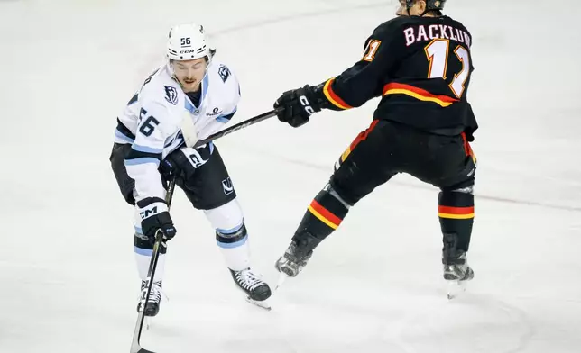 Utah Mammoth's Kailer Yamamoto, left, is hit on the chest by the stick of Calgary Flames' Mikael Backlund, right, during first-period NHL hockey game action in Calgary, Alberta, Saturday, Dec. 6, 2025. (Jeff McIntosh/The Canadian Press via AP)
