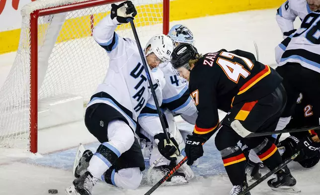Utah Mammoth's Lawson Crouse, left, tries to get the puck away from Calgary Flames' Connor Zary (47) during first-period NHL hockey game action in Calgary, Alberta, Saturday, Dec. 6, 2025. (Jeff McIntosh/The Canadian Press via AP)