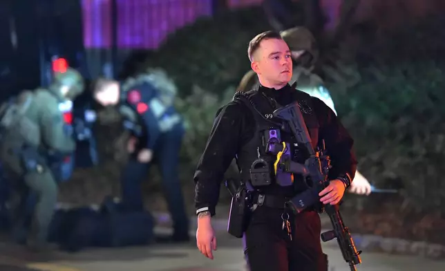 A law enforcement official carries a rifle in a neighborhood near Brown University, Saturday, Dec. 13, 2025, in Providence, R.I. during the investigation of a shooting. (AP Photo/Steven Senne)