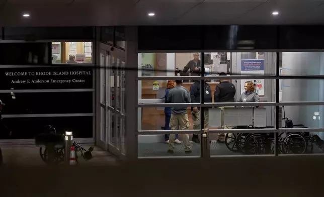 People stand at an entrance to Rhode Island Hospital in Providence, R.I., on Saturday, Dec. 13, 2025, where victims from a shooting at Brown University were transported. (AP Photo/Mark Stockwell)