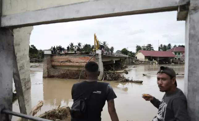 Men sit near a bridge collapsed during a flash flood in Pidie Jaya, Aceh province, Indonesia, Tuesday, Dec. 2, 2025. (AP Photo/Reza Saifullah)