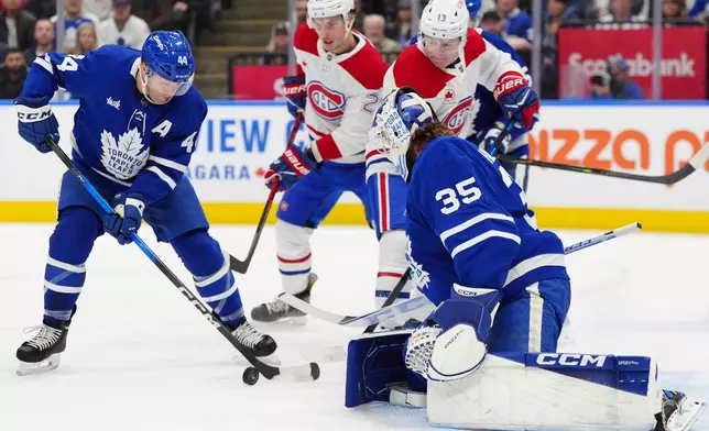 Toronto Maple Leafs defenceman Morgan Rielly (44) clears the puck from in front of his goalie Dennis Hildeby (35) as Montréal Canadiens left wing Juraj Slafkovský (20) and Canadiens right wing Cole Caufield (13) look on during first period NHL hockey action in Toronto on Saturday, Dec. 6, 2025. (Frank Gunn/The Canadian Press via AP)