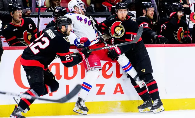 Ottawa Senators' Jordan Spence (10) holds New York Rangers' Alexis Lafreniere, center, against the boards during second-period NHL hockey game action in Ottawa, Ontario, Thursday, Dec. 4, 2025. (Spencer Colby/The Canadian Press via AP)