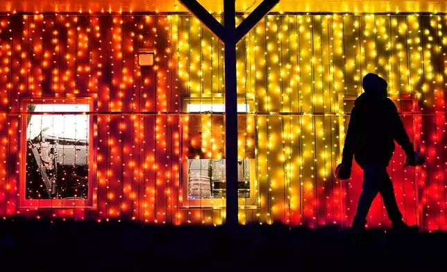 FILE - A person walks past a display of holiday lights on a building at a park in Lenexa, Kan., Dec. 10, 2025. (AP Photo/Charlie Riedel, File)