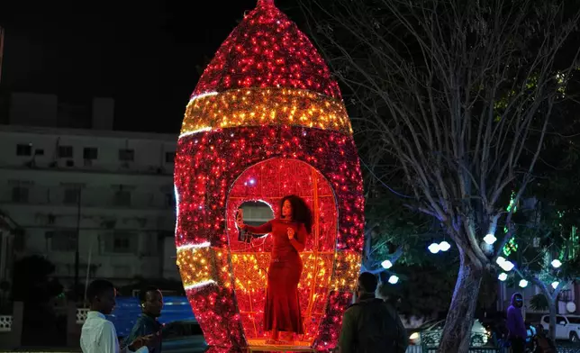 FILE - A woman poses for a selfie inside a giant Christmas ornament illuminated with holiday lights in Dakar, Senegal, Dec. 15, 2025. (AP Photo/Misper Apawu, File)