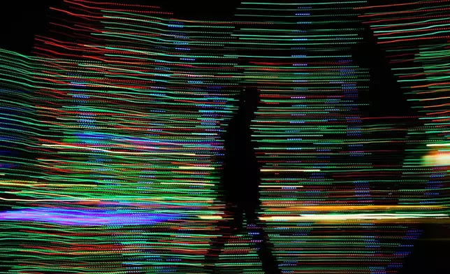 FILE - In this timed exposure a man is silhouetted against holiday lights as he walks by in Lenexa, Kan., Dec. 10, 2025. (AP Photo/Charlie Riedel, File)