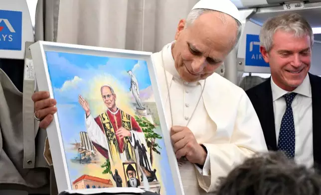 Pope Leo XIV shows a gift he received as he talks to reporters aboard an airplane as he returns from a six-day visit to Turkey and Lebanon, Tuesday, Dec. 2, 2025. (Alessandro Di Meo/Pool Photo via AP)