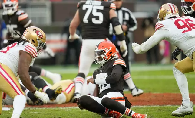 Cleveland Browns quarterback Shedeur Sanders, bottom, slides onto the ground between San Francisco 49ers defensive tackle Kalia Davis, left, and defensive end Clelin Ferrell (96) during the second half of an NFL football game, Sunday, Nov. 30, 2025, in Cleveland. (AP Photo/Sue Ogrocki)
