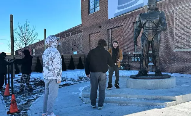 People pose for photos with a RoboCop statue that stands outside a business in Detroit's Eastern Market area, Thursday, Dec. 4, 2025. (AP Photo/Mike Householder)