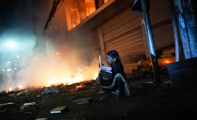 A girl rescues books from a shop near the premises of the Prothom Alo daily newspaper which was set on fire by angry protesters after news reached the country from Singapore of the death of a prominent activist Sharif Osman Hadi, in Dhaka, Bangladesh, Friday, Dec. 19, 2025. (AP Photo/Mahmud Hossain Opu)