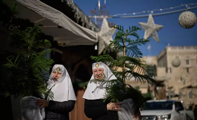Orthodox Christians nuns carry Christmas trees after receiving them during a distribution in the Old City of Jerusalem, Thursday, Dec. 18, 2025, ahead of the Christmas holiday. (AP Photo/Leo Correa)