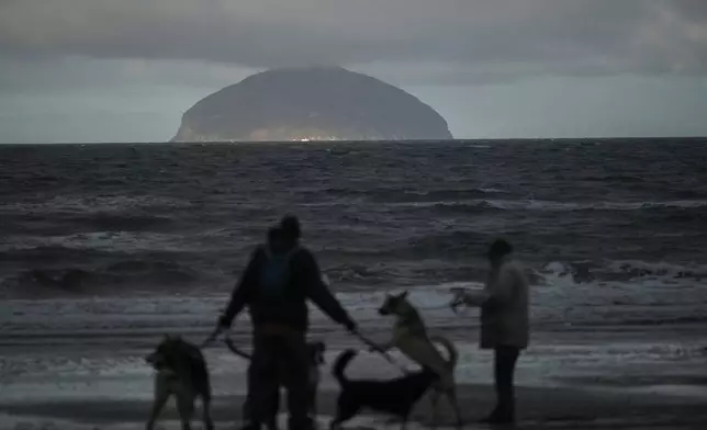 Dog walkers stand on the beach at Girvan with the granite island of Ailsa Craig in the background in Scotland, Thursday, Nov. 13, 2025. (AP Photo/Alastair Grant)