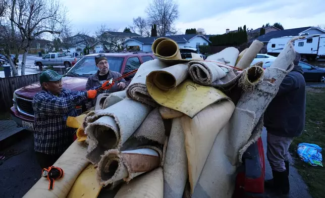 Chanthy Khuon, left, and Bryan Sheriff, second from left, try to secure a large pile of carpet and padding onto a truck after taking it out of the home of Khuon's son after flooding Wednesday, Dec. 17, 2025, in Pacific, Wash. (AP Photo/Lindsey Wasson)
