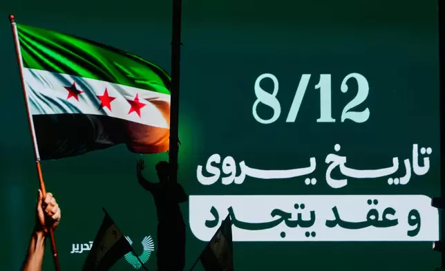 A Syrian man silhouetted by a digital billboard showing the date of the ousting of the Bashar Assad regime during celebrations marking the first anniversary, in Damascus , Syria, Sunday, Dec. 7, 2025. The Arabic words read: "A history retold and a bond renewed." (AP Photo/Hussein Malla)