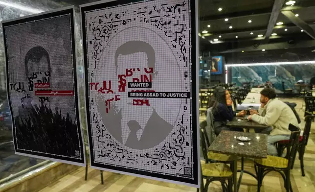 Wanted portraits of former Syrian president Bashar Assad are displayed in the window of a coffeeshop, in Damascus Sunday, Dec. 7, 2025, as Syrians celebrate marking the first anniversary of the ousting of the Bashar Assad regime. (AP Photo/Hussein Malla)