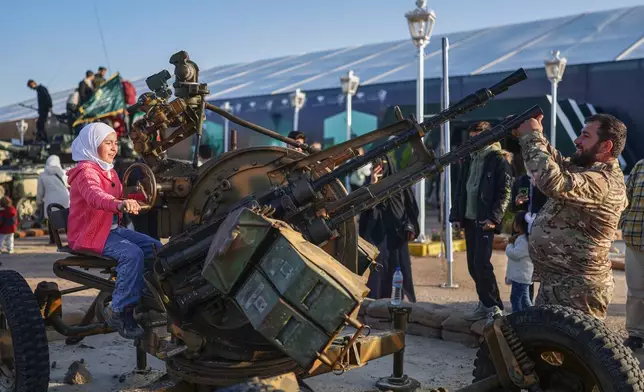 A girl sits on a machine gun as visitors tour the "Syrian Revolution Military Exhibition," which opened last week ahead of the first anniversary of the ousting of the Bashar Assad regime in Damascus, Syria, Sunday, Dec. 7, 2025. (AP Photo/Ghaith Alsayed)