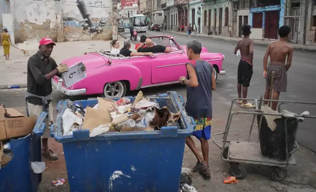 A man collects trash while tourists ride around in a classic American car during a power outage in Havana, Cuba, Wednesday, Dec. 3, 2025. (AP Photo/Ramon Espinosa)