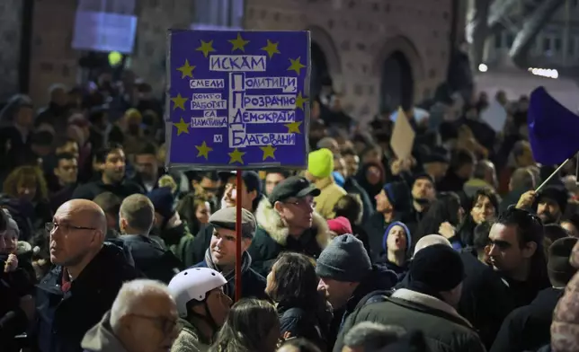 A protester holds a banner as as a swelling crowd of tens of thousands of Bulgarians filled Sofia's central square, demanding the government's resignation amid rising anger over corruption and contested economic policies, Sofia, Bulgaria, Wednesday, Dec. 10, 2025. (AP Photo/Valentina Petrova)