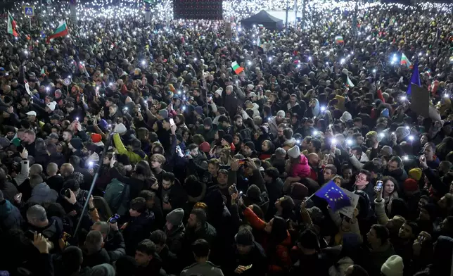 Protesters light their phone's as torches as a swelling crowd of tens of thousands of Bulgarians filled Sofia's central square, demanding the government's resignation amid rising anger over corruption and contested economic policies, Sofia, Bulgaria, Wednesday, Dec. 10, 2025. (AP Photo/Valentina Petrova)