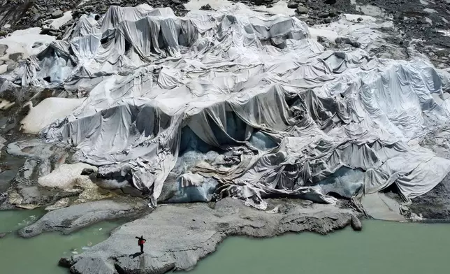 The Rhone Glacier near Goms, Switzerland, is partially covered with sheets as Matthias Huss, head of the Swiss glacier monitoring group GLAMOS, stands nearby, on June 10, 2025. (AP Photo/Matthias Schrader, File)