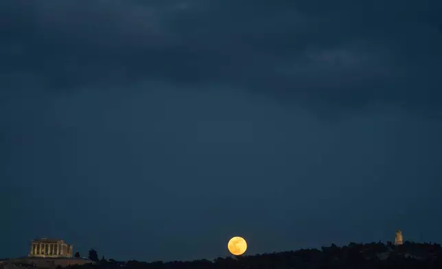 The snow moon rises behind Philopappos Hill, between the Parthenon, left, and the Philopappos Monument, right, in Athens, Greece, on Feb. 12, 2025. (AP Photo/Petros Giannakouris, File)