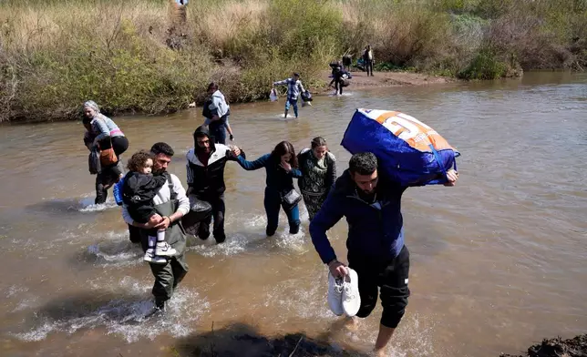 FILE - Syrian Alawite families who fled the clashes in Syria carry their luggage as they cross a river marking the border between Syria and northern Lebanon near the village of Heker al-Daher in Akkar province, Lebanon, March 11, 2025. (AP Photo/Hussein Malla, File)