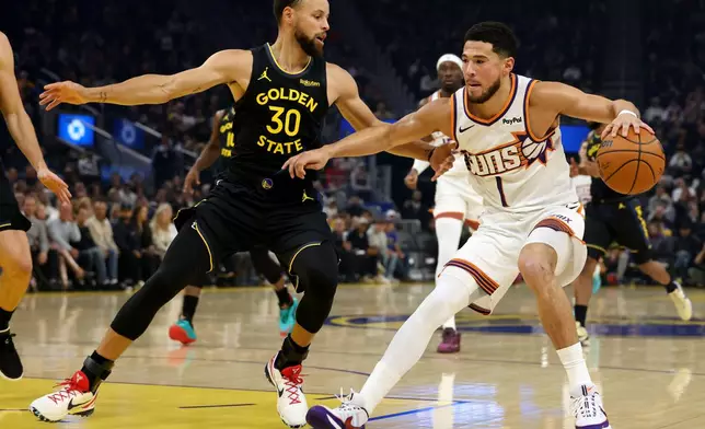 Phoenix Suns guard Devin Booker (1) drives to the basket against Golden State Warriors guard Stephen Curry (30) during the first half of an NBA basketball game in San Francisco, Saturday, Dec. 20, 2025. (AP Photo/Jed Jacobsohn)