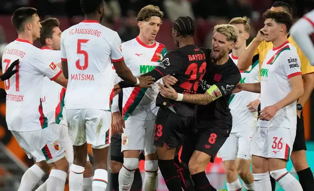 Leverkusen's Robert Andrich, right, pushes team mate Nathan Tella besides Augsburg's Kristijan Jakic during the Bundesliga soccer match between FC Augsburg and Bayer Leverkusen in Augsburg, Germany, Dec. 6, 2025. (AP Photo/Matthias Schrader)