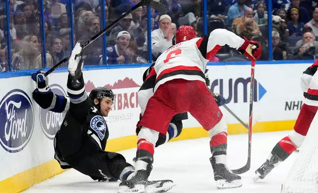 Tampa Bay Lightning center Dominic James (17) gets knocked down by Carolina Hurricanes defenseman Mike Reilly (6) during the second period of an NHL hockey game Saturday, Dec. 20, 2025, in Tampa, Fla. (AP Photo/Chris O'Meara)