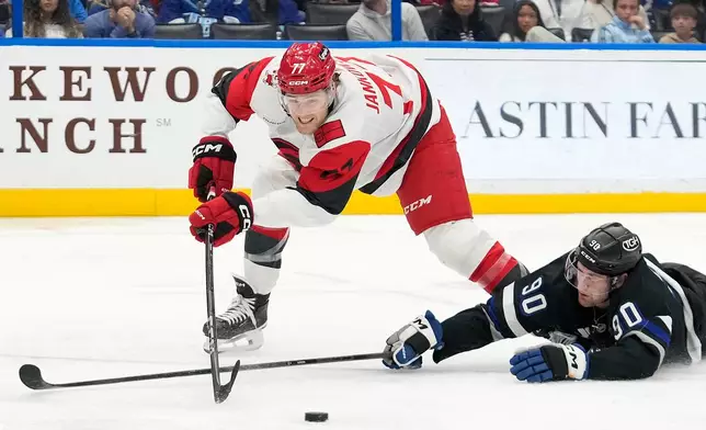 Tampa Bay Lightning defenseman J.J. Moser (90) kncoks the puck away from Carolina Hurricanes left wing Mark Jankowski during the third period of an NHL hockey game Saturday, Dec. 20, 2025, in Tampa, Fla. (AP Photo/Chris O'Meara)