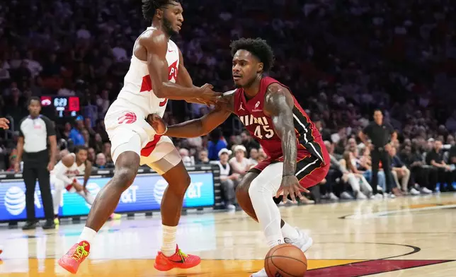 Miami Heat guard Davion Mitchell (45) drives to the basket as Toronto Raptors guard Immanuel Quickley, left, defends during the first half of an NBA basketball game, Tuesday, Dec. 23, 2025, in Miami. (AP Photo/Lynne Sladky)